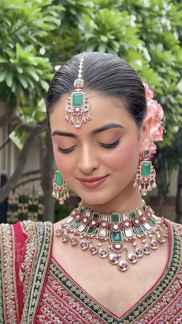 Bride in kundan and emerald jewellery with roses pinned into her hair, soft glowing skin