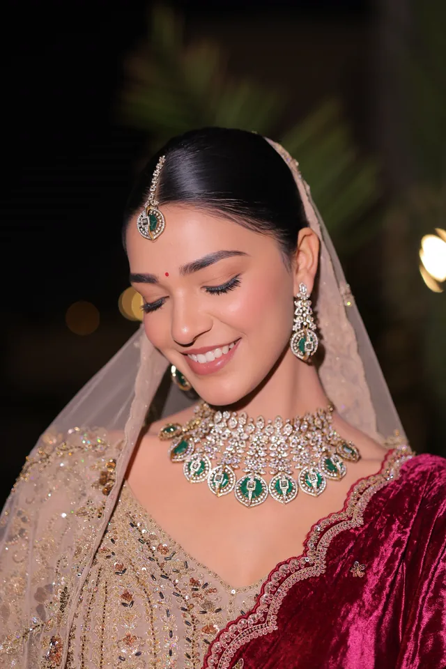 Bride smiling in an emerald choker and blush dupatta, photographed at night
