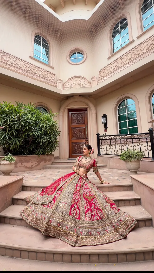 Bride in a red and gold lehenga fanned across sandstone steps of a haveli courtyard