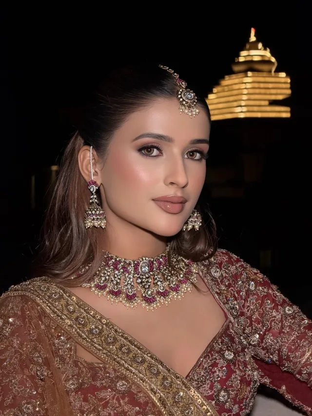 Bride in an embroidered mauve lehenga against a domed rooftop at dusk